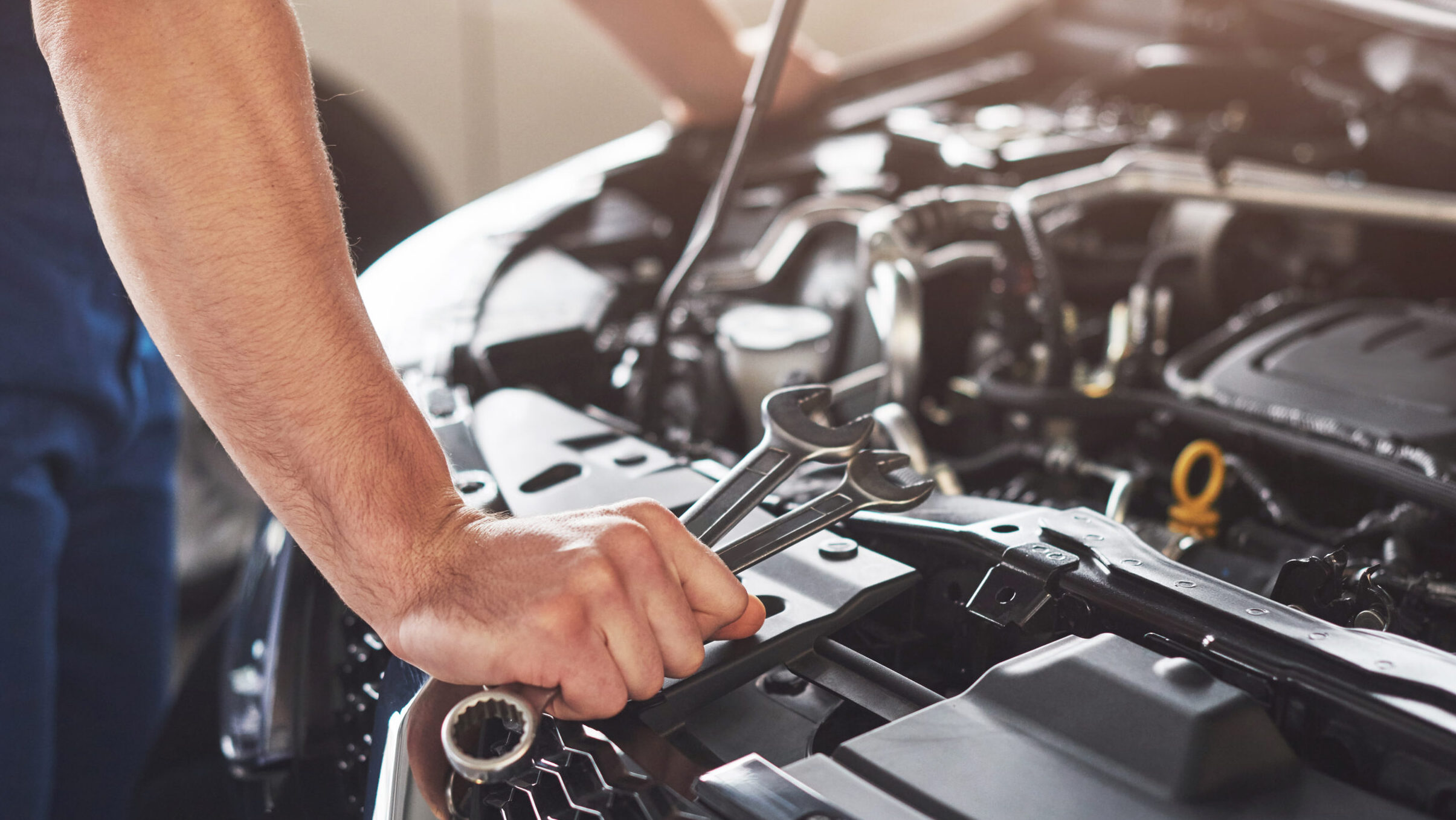 Mechaniker hält Schraubenschlüssel über offenem Motorraum eines Autos