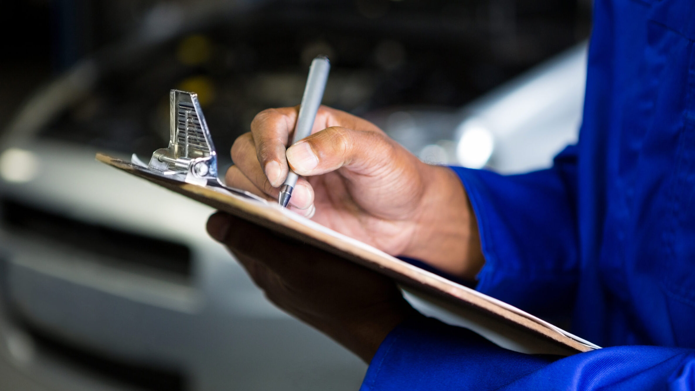 Kfz-Mechaniker überprüft Fahrzeug und dokumentiert Ergebnisse auf einem Klemmbrett